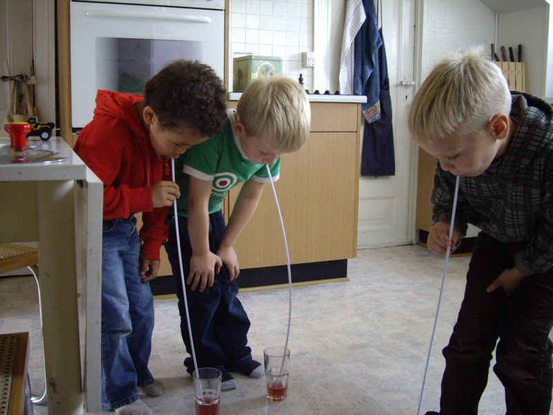 Tre drenge drikker saftevand af meget lange sugerÃ¸r.